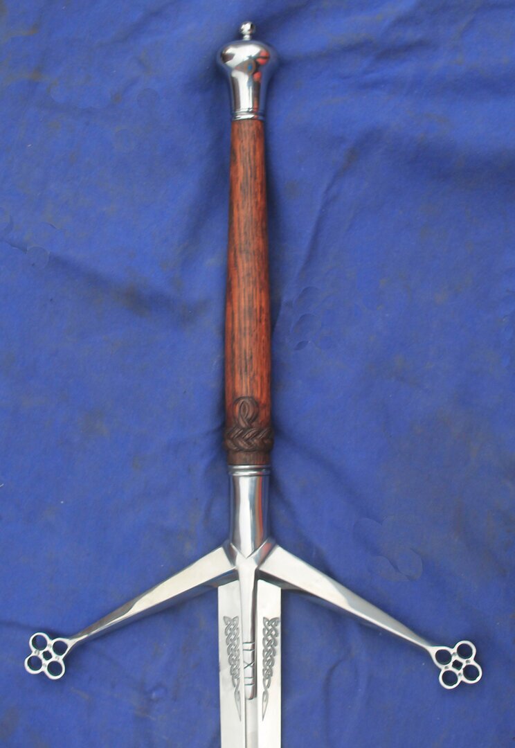 Scottish Claymore. hilt has sloping quillons with quatrafoil terminals.Langets extend down onto the blade and have straight-line markings cut into the surface. Oak grip with carved knotwork  and bulb pommel.
						Blade Dimensions
						Sharp
						105cm Blade  5cm Hilt  2.5cm Tip
						Reenactment
						105cm Blade  5cm Hilt  2.5cm Tip