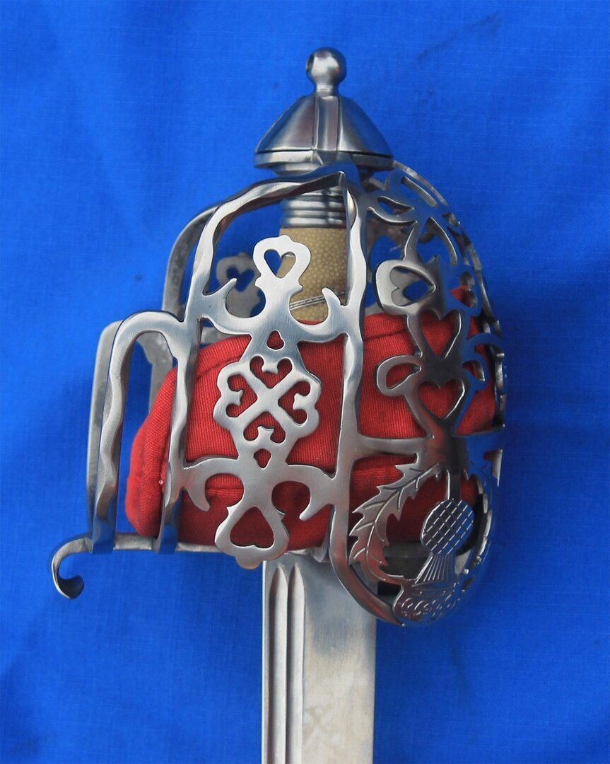 Side view of satin finished basket with wavy bars and complex piercings, has thistle decoration over the sword catchers. Has a red linen over leather liner. Comes with Shark Skin grip with brass or silver wire .