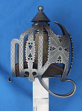 Acid Etched Scottish Basket
						Comes with Shark Skin grip with brass or silver wire 
						and liner. Triangle and circle cut outs on the hilt and etched knotwork swirls and swords on the bars and panels.